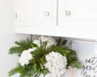 Winter white large head hydrangeas and greenery mixed in a white pitcher becomes cheery winter decor.