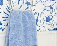 blue hand towel hanging on towel hook in bathroom. Towel is embellished with blue and white fabric and ribbon.