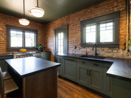U-shaped large green kitchen with inset cabinets, vintage elements and dark brown island with black granite countertops and hardware